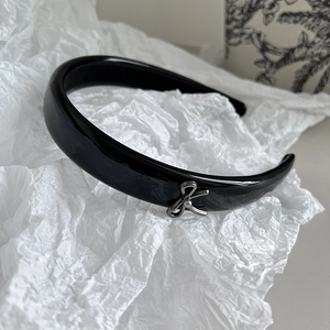 Close-up of black patent leather headband featuring a delicate silver metal bow detail