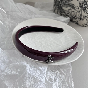 Detailed view of dark purple patent leather headband with silver metal bow on white tray