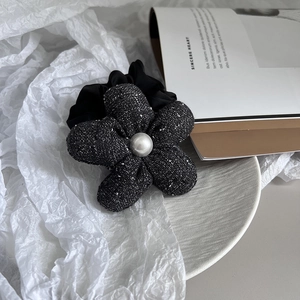 Detailed view of elegant black tweed flower hair tie with central white faux pearl accent