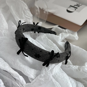 Detail showing grey knit headband with black bows and handmade label on white paper