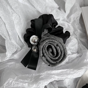 Detail of elegant black satin scrunchie with houndstooth rose and ribbon bow