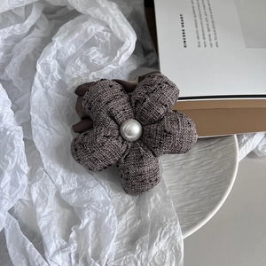 Detail of brown tweed flower hair tie with a central pearl on a white ceramic plate