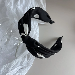 Dettaglio di un cerchietto retrò in raso nero a pois bianchi con un elegante nodo a torsione