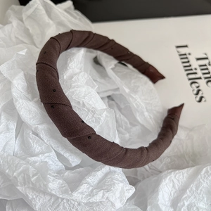 Detail eines dunkelbraunen Wollstirnbands mit schwarzen Punkten und Knotendesign