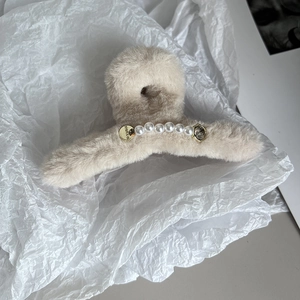 Détail d'une pince à cheveux en peluche beige avec perles blanches et logo doré