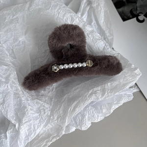 Détail d'une pince à cheveux en peluche marron avec perles blanches et plaque dorée élégante