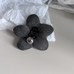 Detail of elegant black flower hair claw with shimmering fabric and silver center