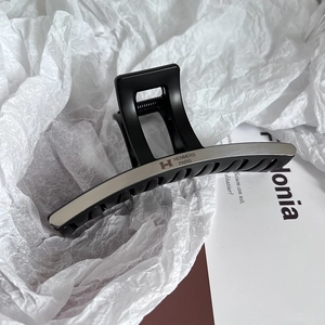 Detail of matte black large hair claw clip with brushed silver H logo metal insert