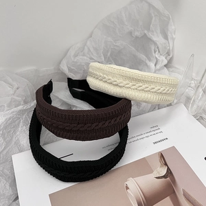 Trois serre-têtes en maille torsadée de couleur crème, marron et noir sur fond élégant