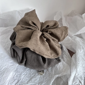 Close-up of oversized pleated fabric scrunchies with circular metal pendant detail