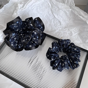 Detail of navy blue floral scrunchies set with black satin trim on a glass tray