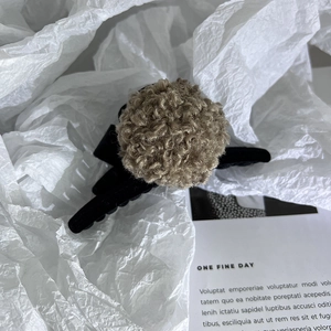 Vue détaillée de la pince à cheveux noire avec un pompon en peluche marron doux