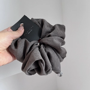 Detailed close-up of a charcoal grey velvet scrunchie with a silver pendant and brand tag