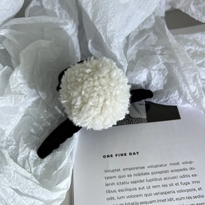 Détail d'une pince à cheveux noire avec des pompons en fausse fourrure blanche et ressort