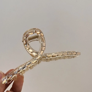 Close-up of champagne crystal hair claw clip with cross-twist design and strong metal spring