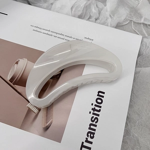 Détail d'une grande pince à cheveux crème en forme de croissant sur un fond magazine
