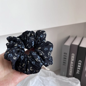 Detailed close-up of a black floral scrunchie with soft fabric and blue flower patterns