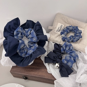 Detail of dark blue denim hair ties with white daisy embroidery and a heart pendant