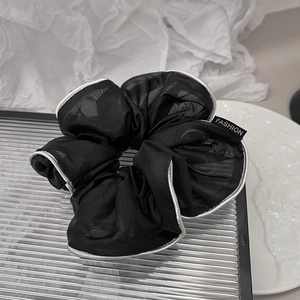 Close-up of black organza scrunchie with silver edges and Fashion label on glass
