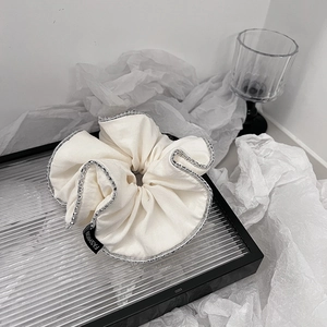 Dettaglio scrunchie in tessuto bianco con perline argento e etichetta Fashion su vassoio