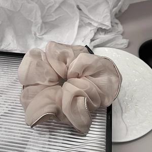 Close-up of champagne organza oversized scrunchie with silver piping and fashion label