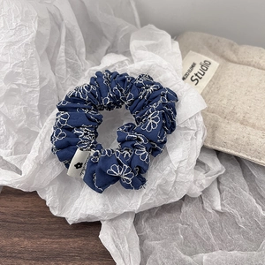 Detail shot of navy blue denim scrunchie featuring white daisy floral embroidery textures