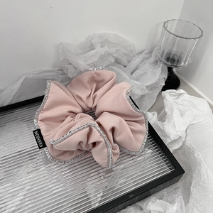 Dettaglio scrunchie in tessuto rosa con bordo a lettere ed etichetta moda su vassoio vetro
