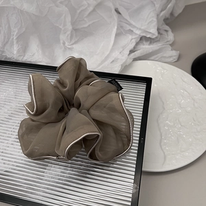 Detailed view of dark brown organza scrunchie with silver piping on a textured tray