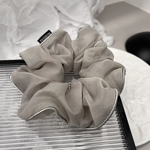 Close-up of grey organza scrunchie with silver piping and fashion label on a white dish