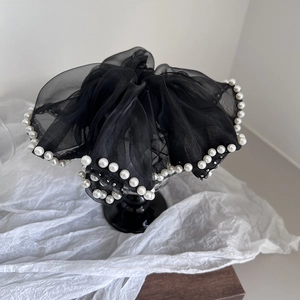 Détail d'un chouchou en organza noir orné de perles blanches sur support élégant