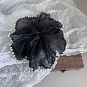 Détail d'un chouchou en tulle noir avec bordure en perles blanches sur fond texturé