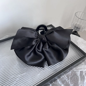 Détail d'une pince à cheveux avec nœud en satin noir sur un plateau en verre