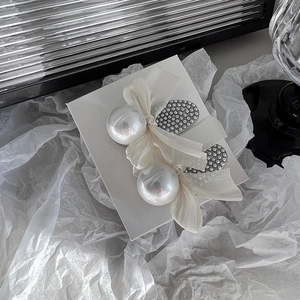 Detailed macro view of white faux pearl and organza bow hair clip on display card