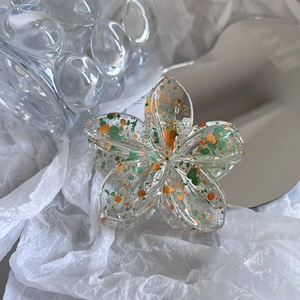 Detailed macro view of plumeria flower hair claw with orange and green paint splatters