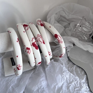 Puffy cream headbands with red cherry patterns and bows on a grey display stand