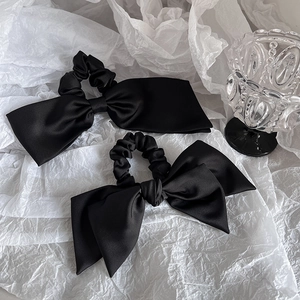 Detail von eleganten schwarzen Satin-Haargummis mit Schleifen auf ästhetischem Hintergrund
