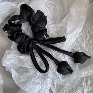 Détail d'un chouchou en satin noir avec perles blanches, strass et ruban à nœud