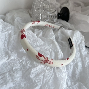 Close-up of cream fabric headband with red cherry patterns and Hand Made woven label