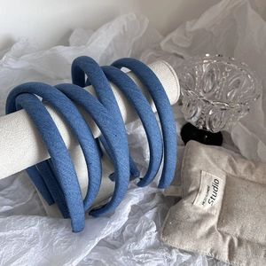 Set of six slim denim blue fabric headbands displayed on a minimalist jewelry stand