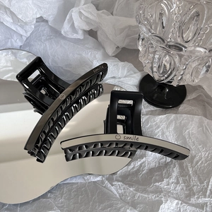 Grande pince à cheveux noire élégante avec logo smile argenté sur miroir minimaliste
