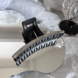 Pince à cheveux en acier titane noir mat avec gravure smile sur une surface miroir chic