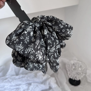 Detailed view of large black floral scrunchie with pleated chiffon fabric and tiny white buds