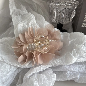 Close-up of elegant beige chiffon flower hair claw clip on soft white textured background