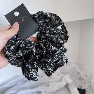 Detailed view of a black floral scrunchie with white flower print and designer tag