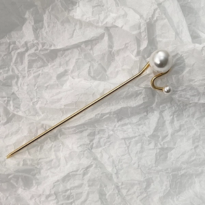 Vue détaillée du pic à cheveux doré avec courbes élégantes et deux perles blanches