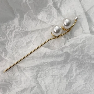 Détail d'un pic à cheveux minimaliste en métal doré avec trois perles élégantes