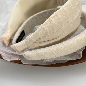 Close-up of dual textures showing satin and jacquard beige sponge headbands with handmade labels