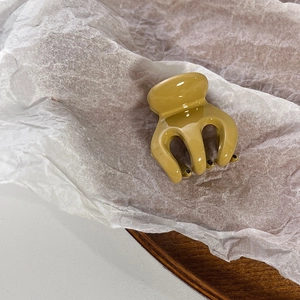 Macro shot of glossy mustard yellow mini hair claw clip on white textured paper