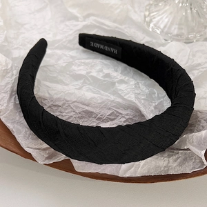 Detailed view of black pleated sponge headband featuring a woven Hand Made label tag