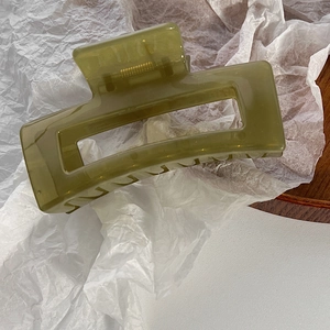 Dettaglio molletta per capelli verde oliva con molla dorata su vassoio di legno